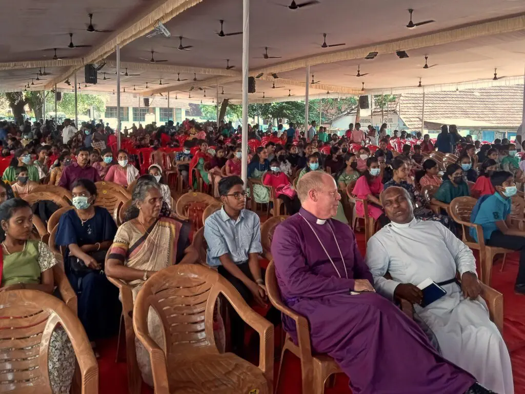 Bishop Andrew chatting at the front of a large group of people.