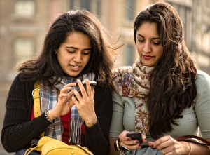 Two young women look at their mobile phones.