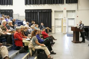 The Rev. Jeffrey Metcalfe speaks to an audience in a theatre.