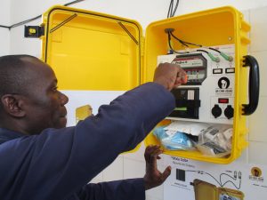 A man installs a device housed in a yellow container that looks like a suitcase.