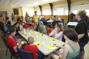 Children and teens enjoy a snack sitting around a table together.