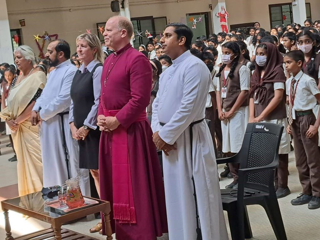 Bishop Andrew and Mary Asbil stand in a congregation of students.