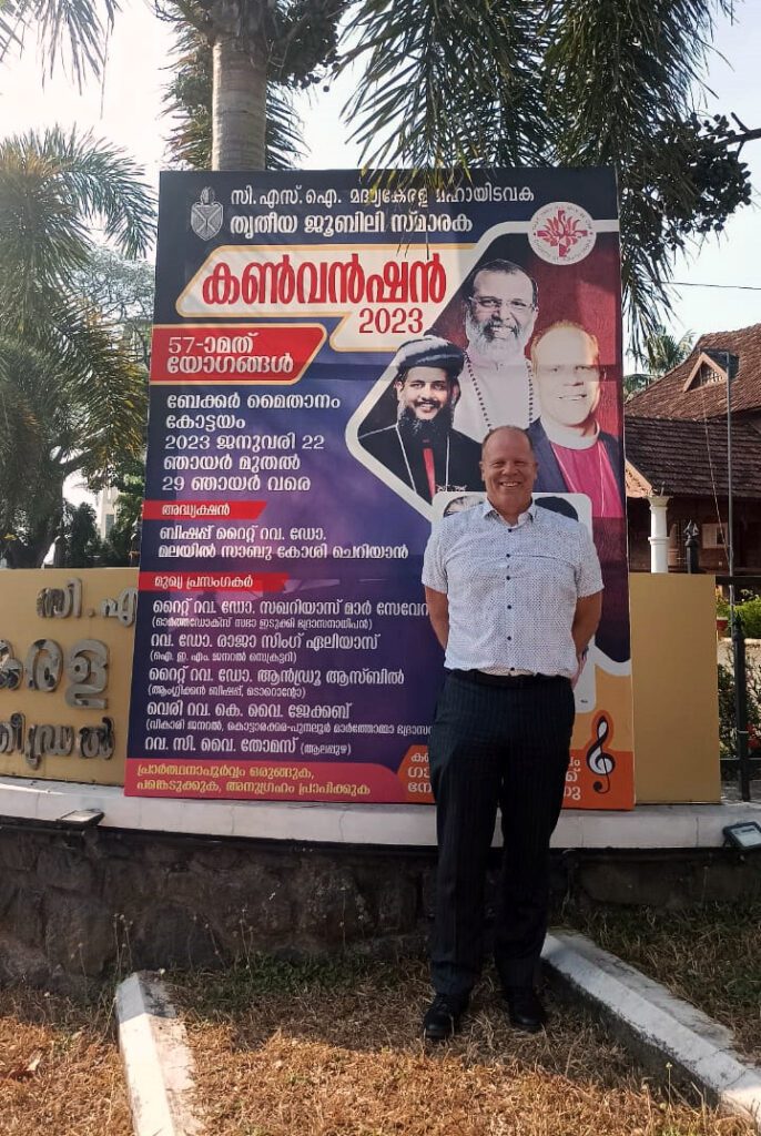 Bishop Andrewtanding in front of a billboard advertising the convention.